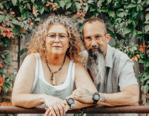 Chris and Laurie, co-owners of Lunara Expeditions, smiling together while leaning on a railing in front of a wall covered in green and red ivy.